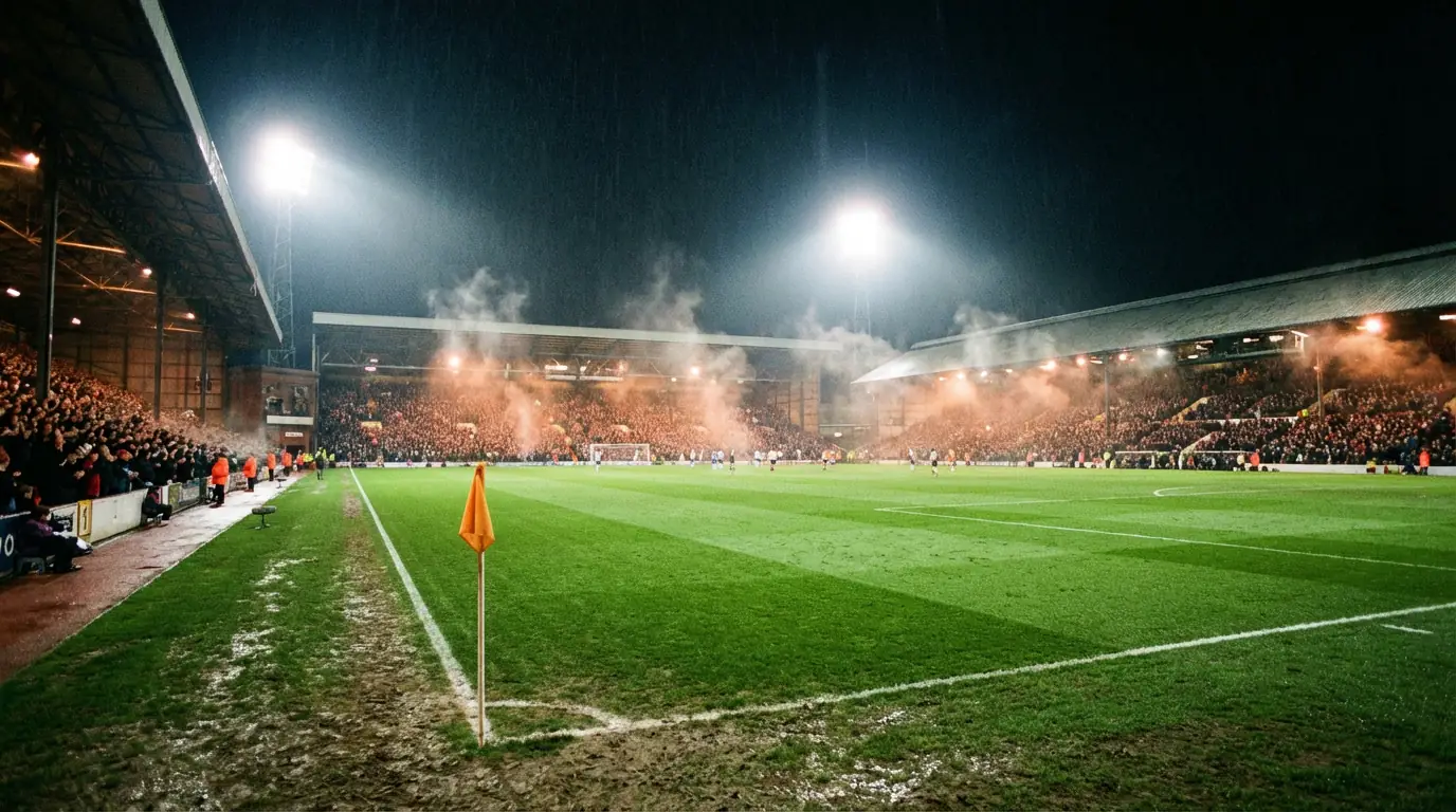 Stadio di calcio inglese con campo in erba verde illuminato sotto i riflettori durante una partita serale