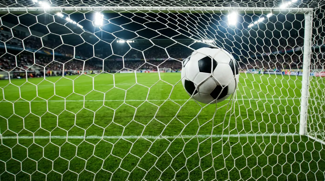 Pallone da calcio che entra in rete visto da dietro la porta su un campo in erba illuminato